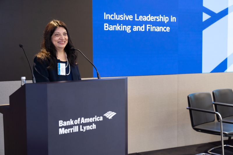 woman in pearls smiles on stage during presentation