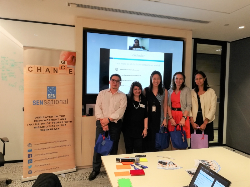 4 women and 1 man standing up in front of an event banner and presentation in a corporate board room setting