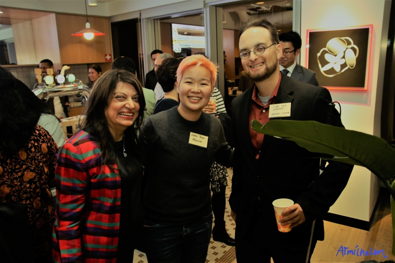 two women, one with orange hair, are smiling and standing next to a man with glasses who is also smiling