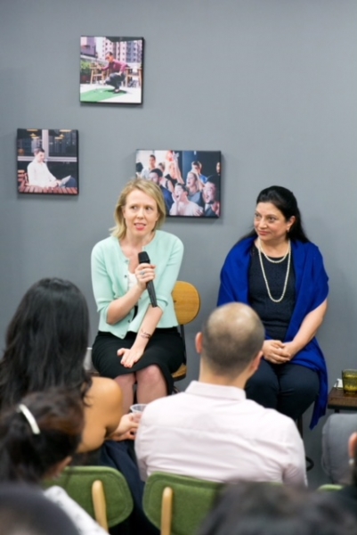 2 women in business attire are speaking as panel members, audience members can be seen at the bottom of the photo sitting in rows.