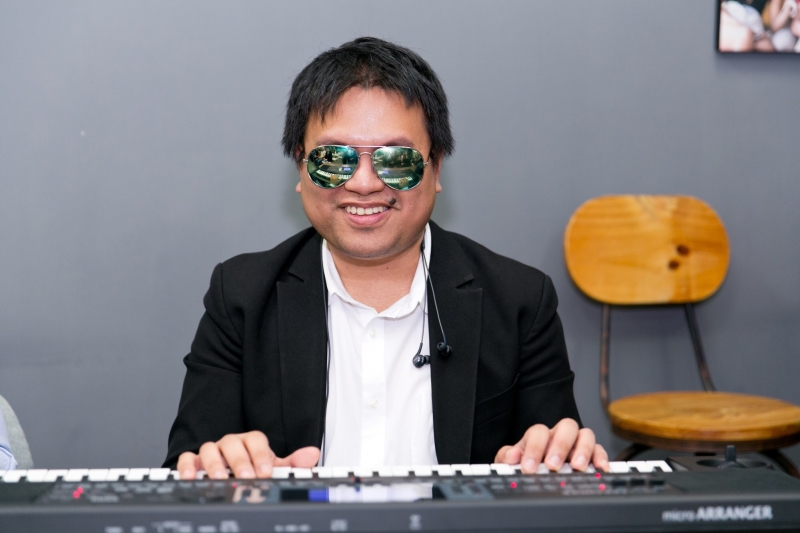 A visually impaired man in a suit is sitting behind a piano and is performing for everyone in attendance