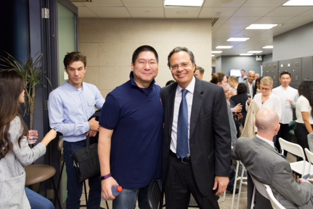 2 men are grouped together for a photo, in the background the remaining audience members can be seen networking with each other.