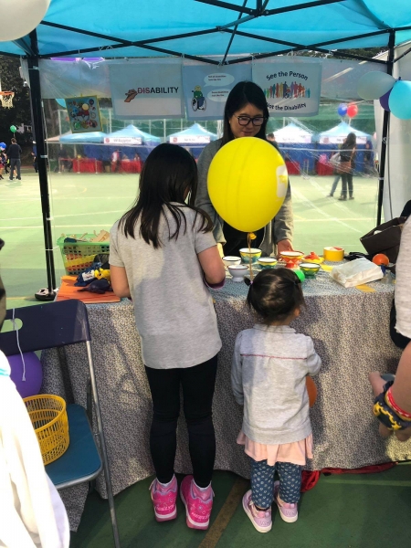 2 girls can be seen standing in front of a stall that aims to raise disability awareness, behind the stall a woman can be seen talking to the girls