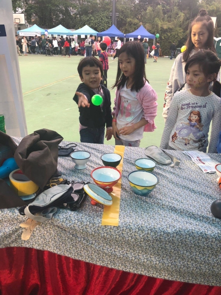 A boy is trying to throw a small green ball into a cup, to his side, 3 girls can be seen watching him