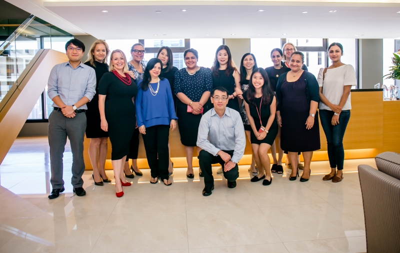Skadden and SENsational staff members dressed in business attire are standing in front of the reception desk for a group photo
