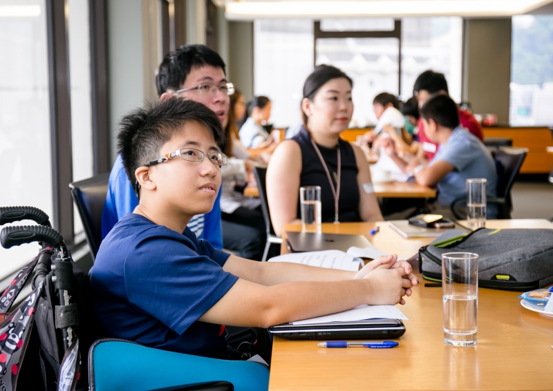 A Skadden staff member in business attire is seated with participants of the training seminar whilst by attention to an off-picture presentation