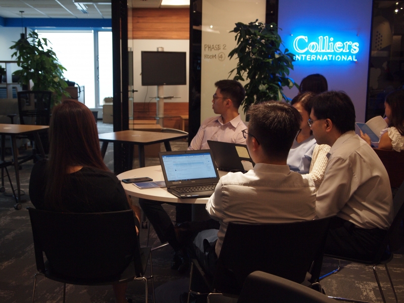 A group of men and women in business attire sitting at a table listening to a presentation.