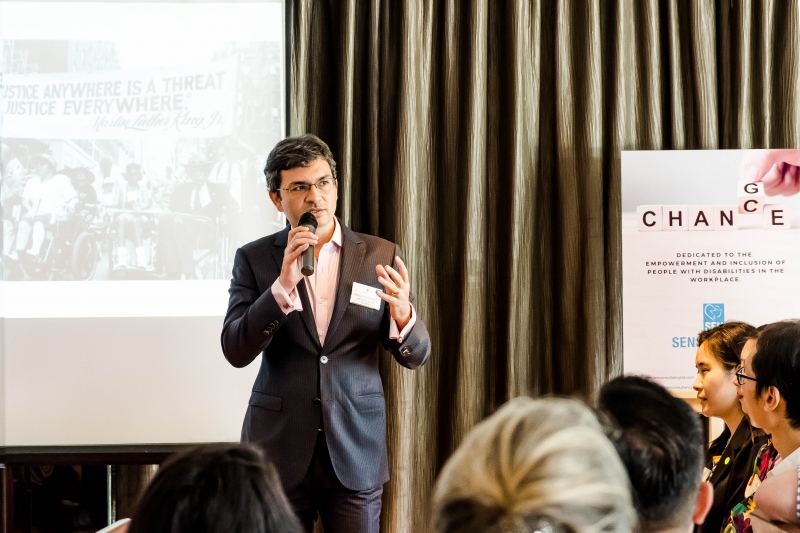 A man wearing glasses and a suit is speaking to an audience