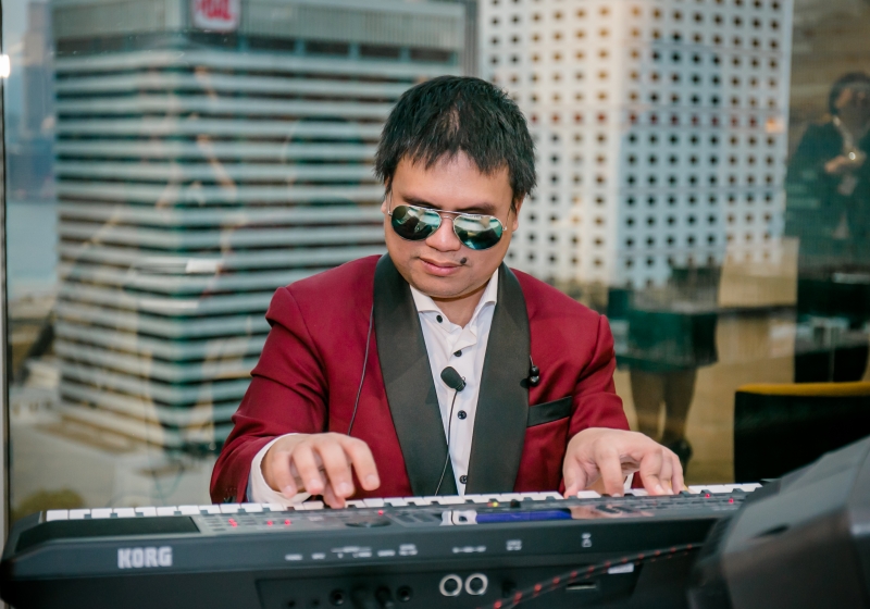 A visually impaired man in a red suit is seated behind the piano and performing a song.