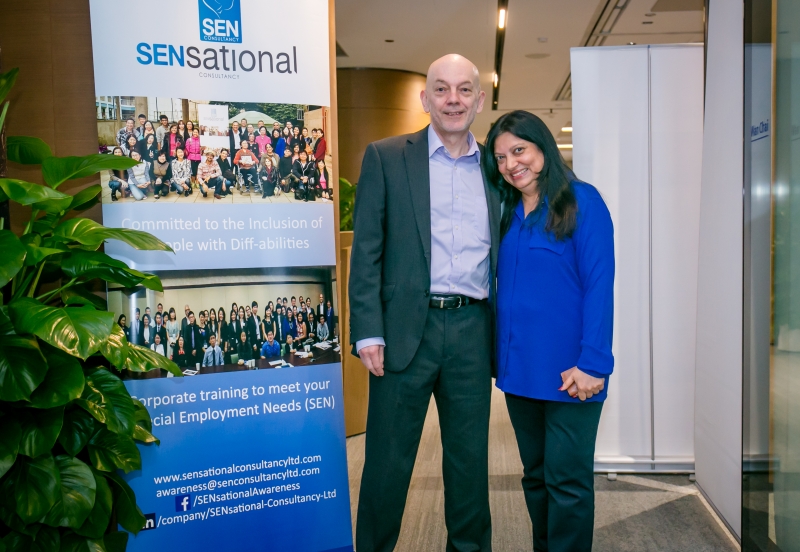 A man and a woman in business attire posing for a photo next to a SENsational banner