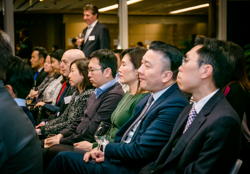 Audience members all dressed in business attire can be seen seated in rows whilst listening to the panel discussion