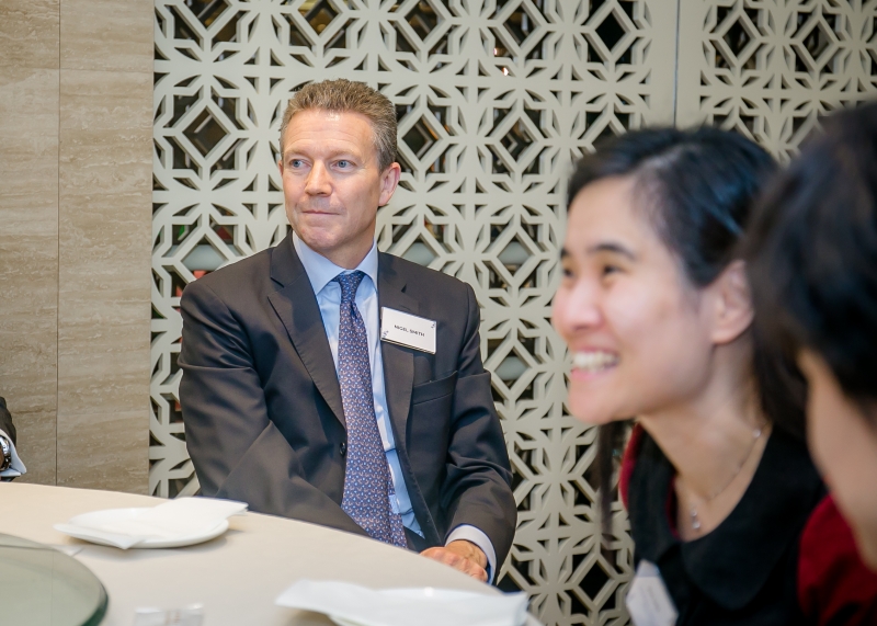A photo focus on a man in a suit with 2 women out of focus in the background