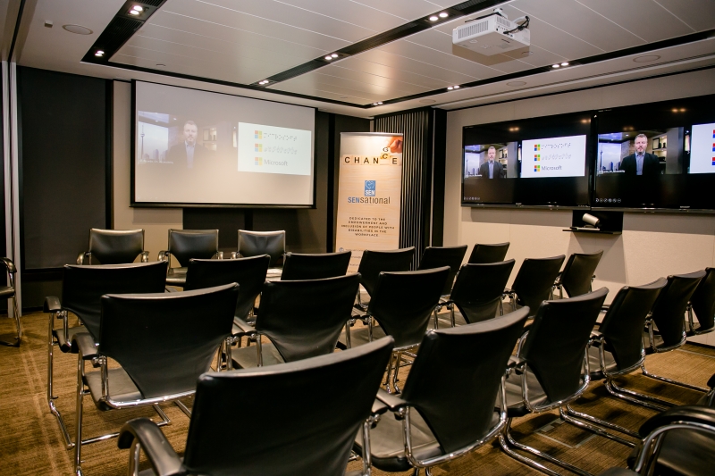 3 chairs (for the panelists) facing a row of chairs with two screens one behind the panelist chairs and one to the right of the audience