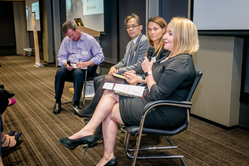 2 men and 2 women in business attire sitting on chairs speaking to the audience