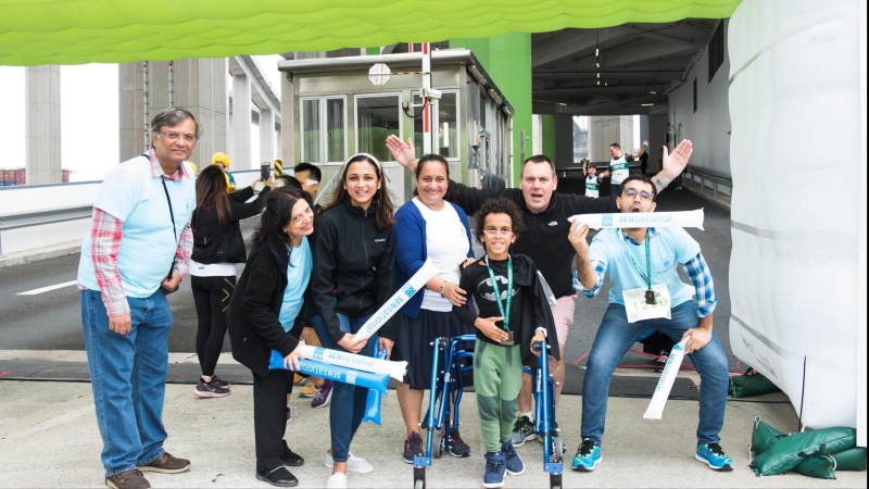 a group of people laugh and pose, including a child in a batman outfit using a walker