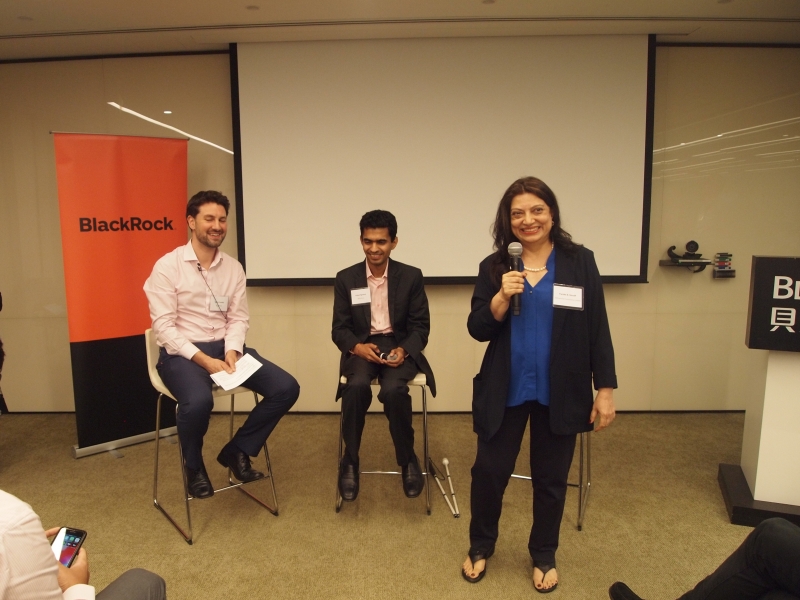 woman stands presenting in front of two male panelists